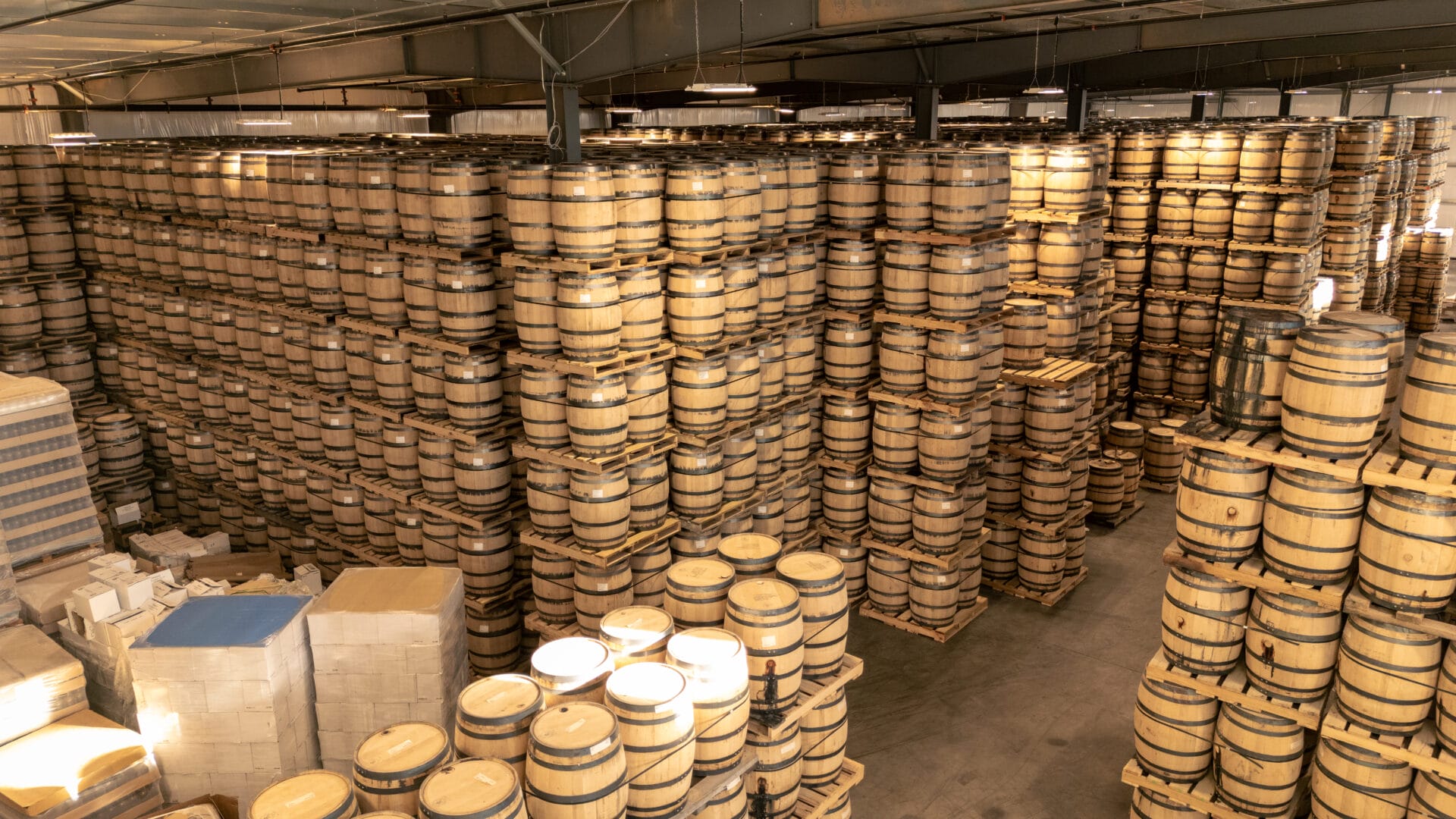 A large warehouse at Old Glory Distilling Co., filled with neatly stacked wooden barrels used for aging whiskey. The barrels are arranged in high stacks, showcasing the scale of production and the traditional aging process. Warm lighting highlights the natural wood tones of the barrels.